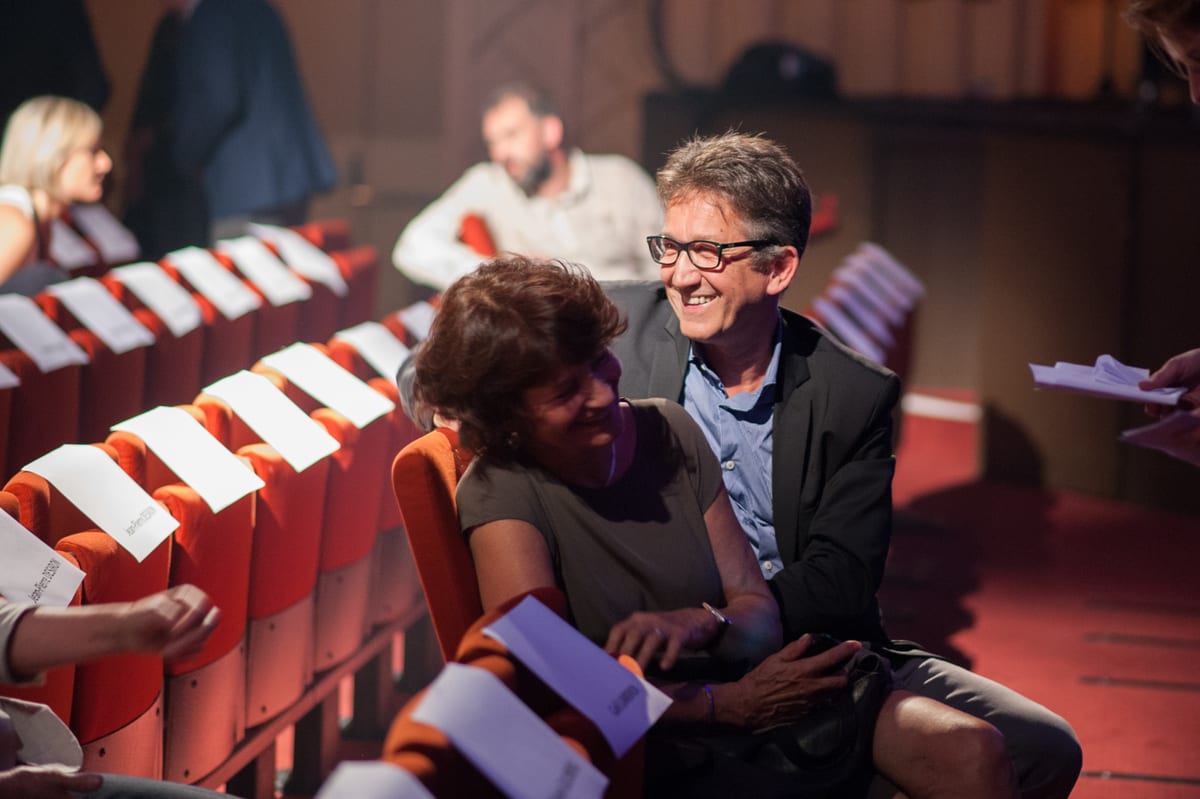 Couple complice riant dans les fauteuils rouges d'une salle de spectacle, programme en main