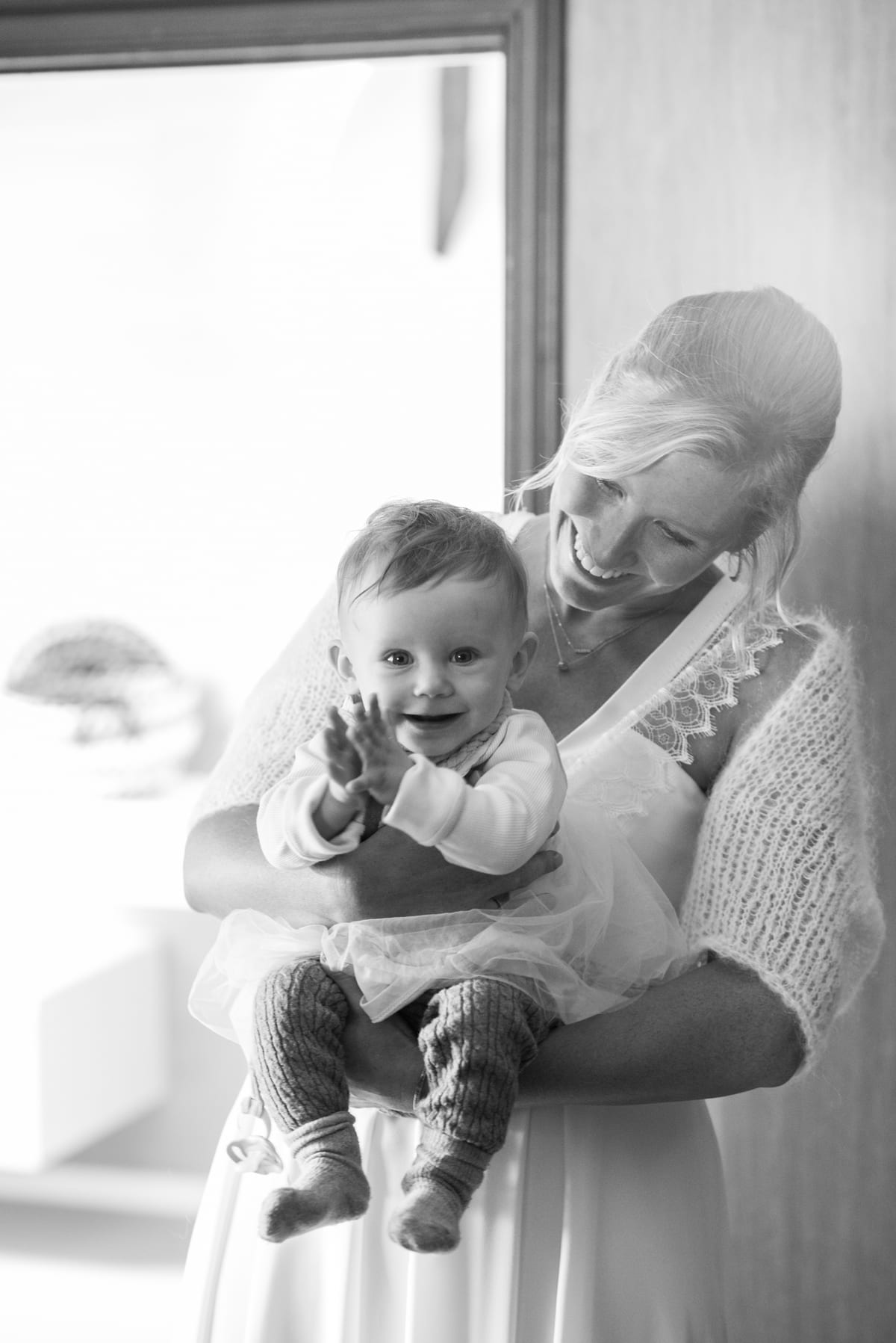 Mariée portant un bébé rieur qui tend la main vers l'objectif, en noir et blanc