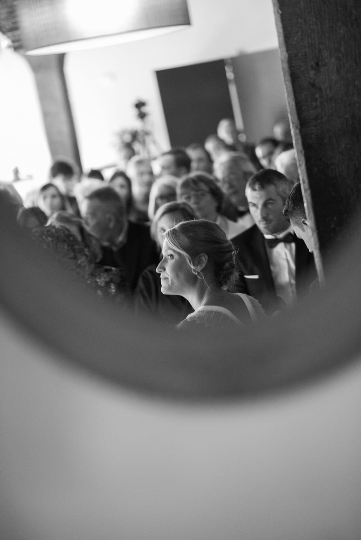 Mariée de profil au milieu de l'assistance, aperçue à travers une ouverture circulaire, en noir et blanc