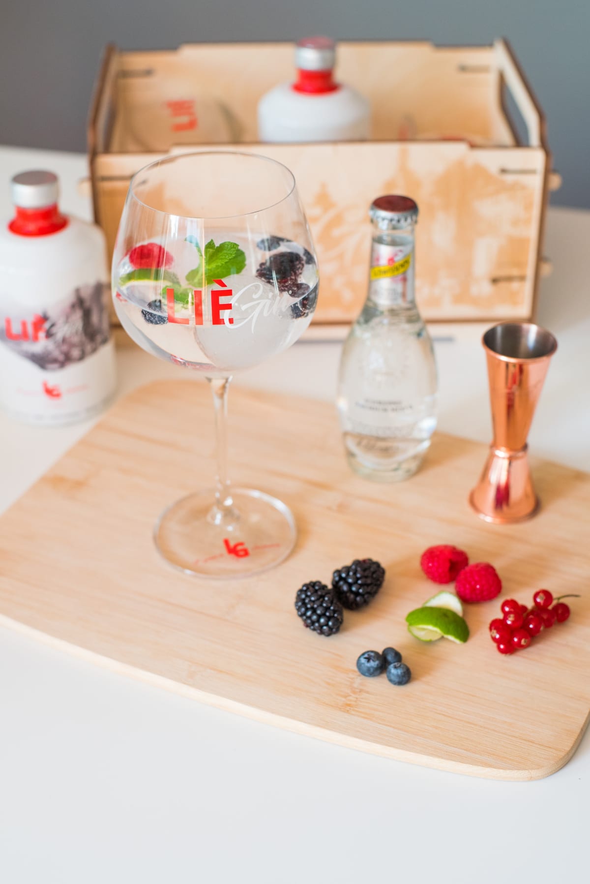 Nature morte de cocktail : verre garni de fruits rouges, bouteille de gin et coffret en bois clair