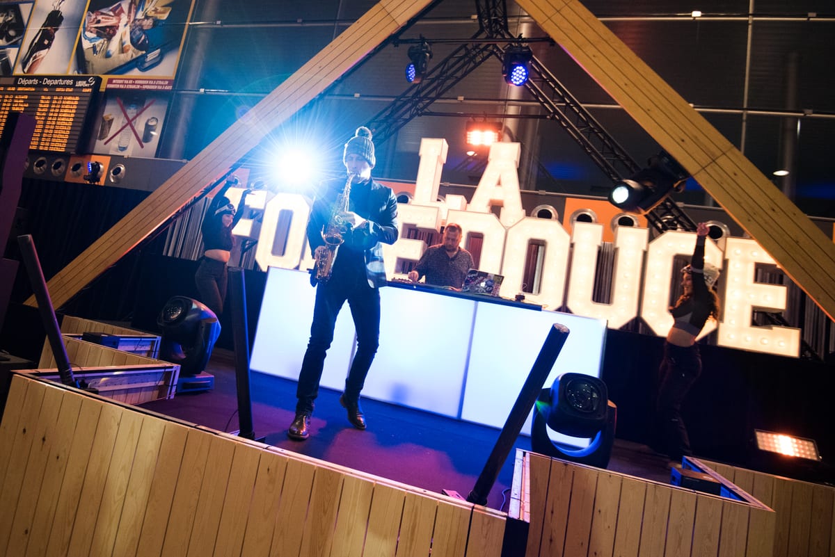 Saxophoniste en contre-jour devant de grandes lettres lumineuses, sur une scène de soirée