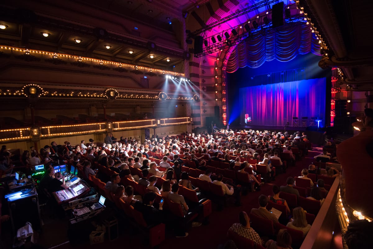Salle de théâtre à l'italienne comble, vue depuis un balcon vers la scène éclairée