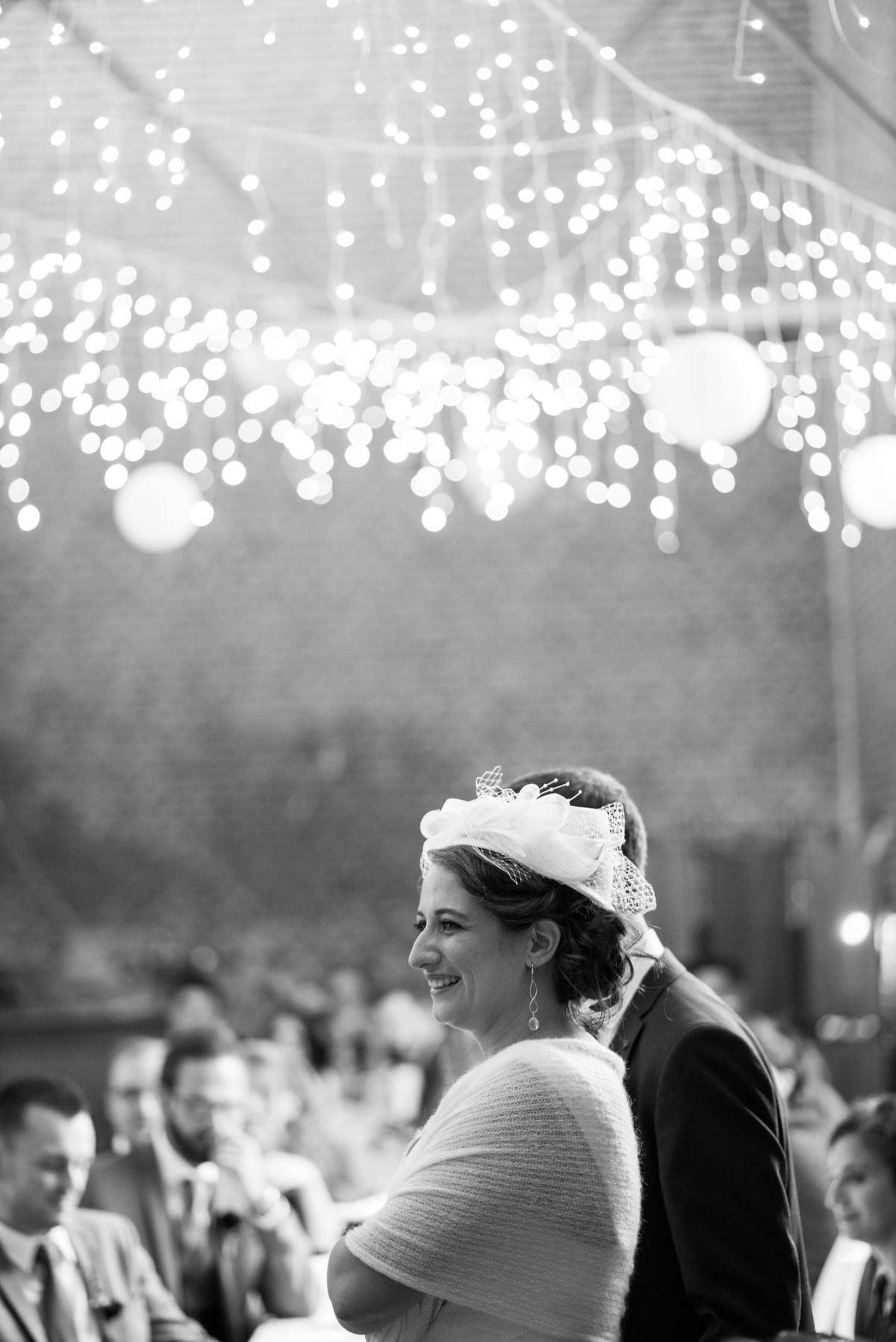 Mariée souriante sous un ciel de guirlandes lumineuses et de lampions, en noir et blanc